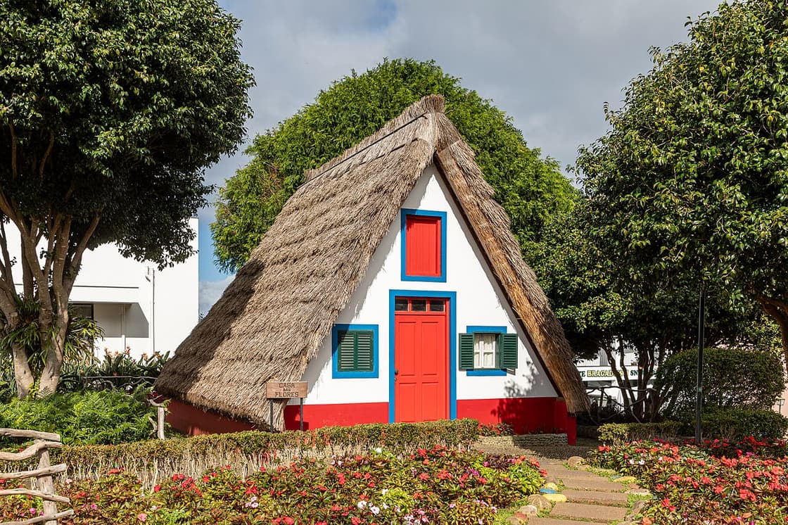 A white, red and blue thatched house in Santana beside the garden paths of a village visit.
